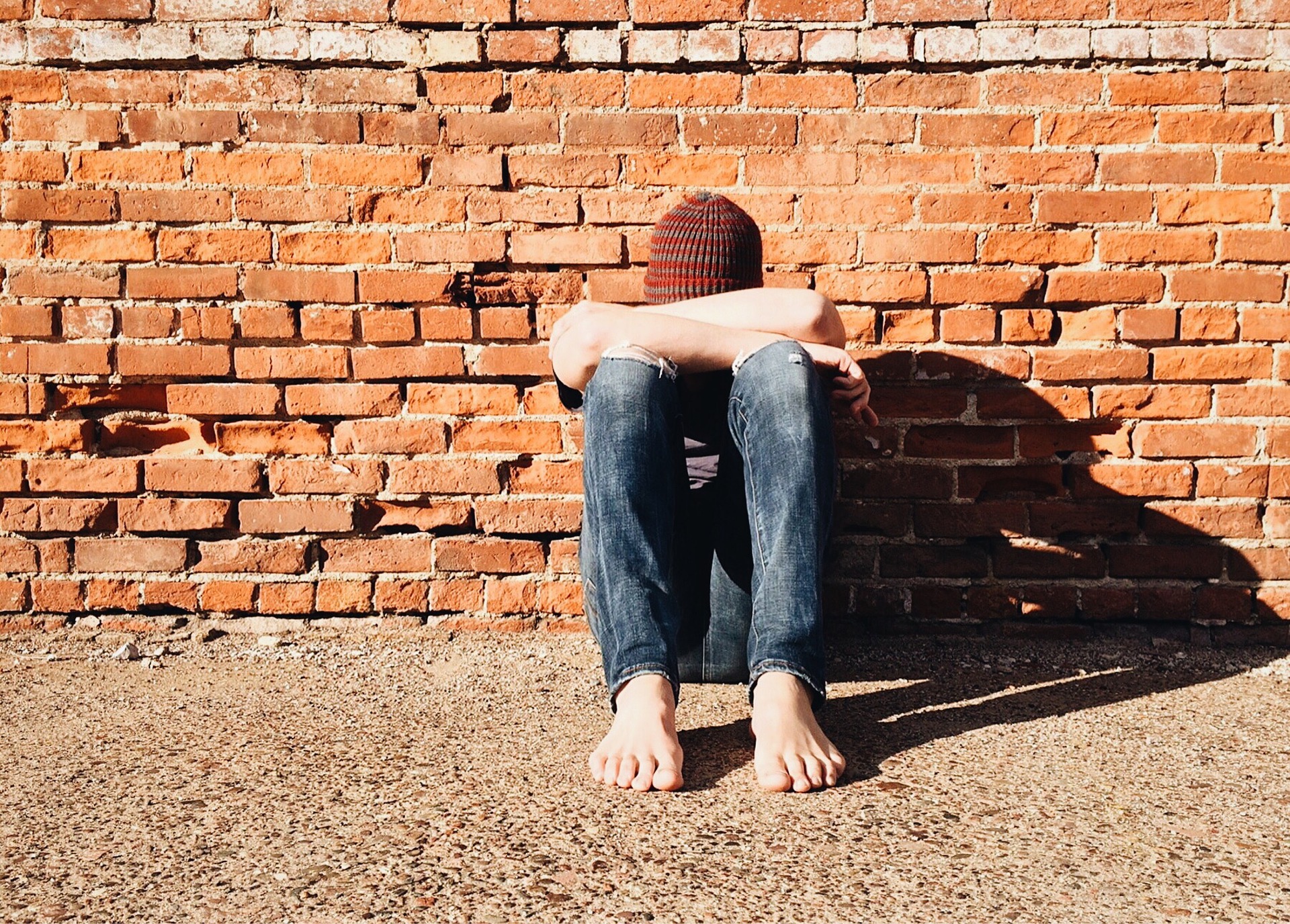 bullied young boy in hat sadly leaning against a wall